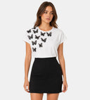 T-shirt blanc ANI ARPÉ en coton avec papillons noirs en relief sur l'épaule, porté avec une jupe noire.