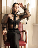 Chemise ANI ARPÉ transparente en plumetis noir avec col montant et ruban noué, portée par une femme assise